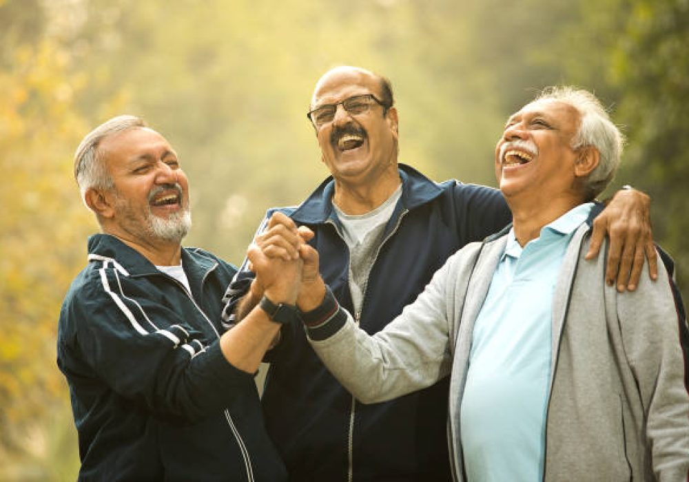 Cheerful old male friends stacking hands together at park